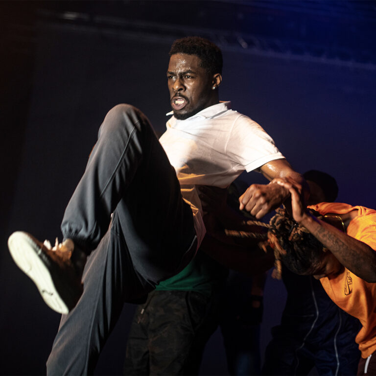 Eine Person of Colour tanzt kraftvoll Krump. Eine weitere Person of Colour tanzt dahinter und hält die erste Person fest.