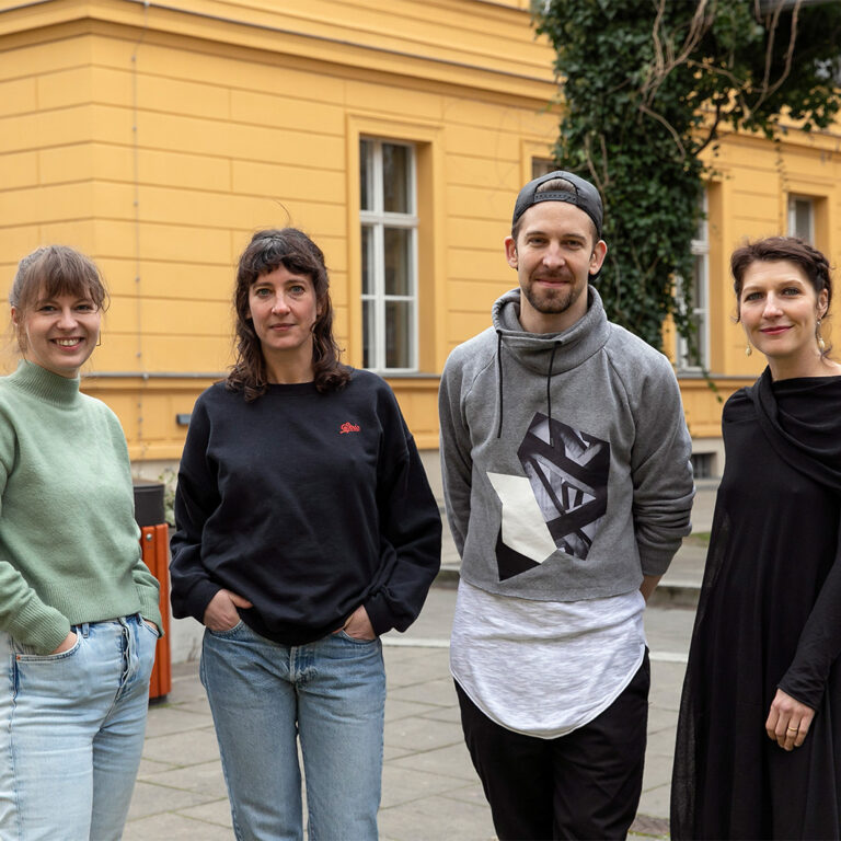 Vier Personen stehen vor einem gelben Haus. Die Bewerber/Autoren/Innen des Berliner Kindertheaterpreises 2023 des Grips Theaters und der Gasag: Marie Huettner, Ayse Bosse, Sebastian Klauke und Julia Blesken (nicht im Bild Lara Schuetzsack). Februar 2022.